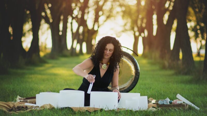 Woman rubbing an arrangement of sound bowls in a lush green forest